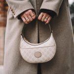 a woman in a coat holding a white purse