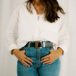 Woman wearing a white shirt, jeans, and a belt.
