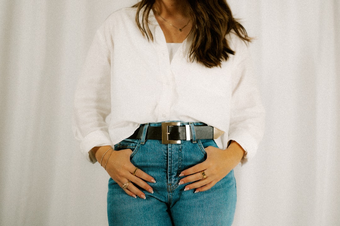 Woman wearing a white shirt, jeans, and a belt.