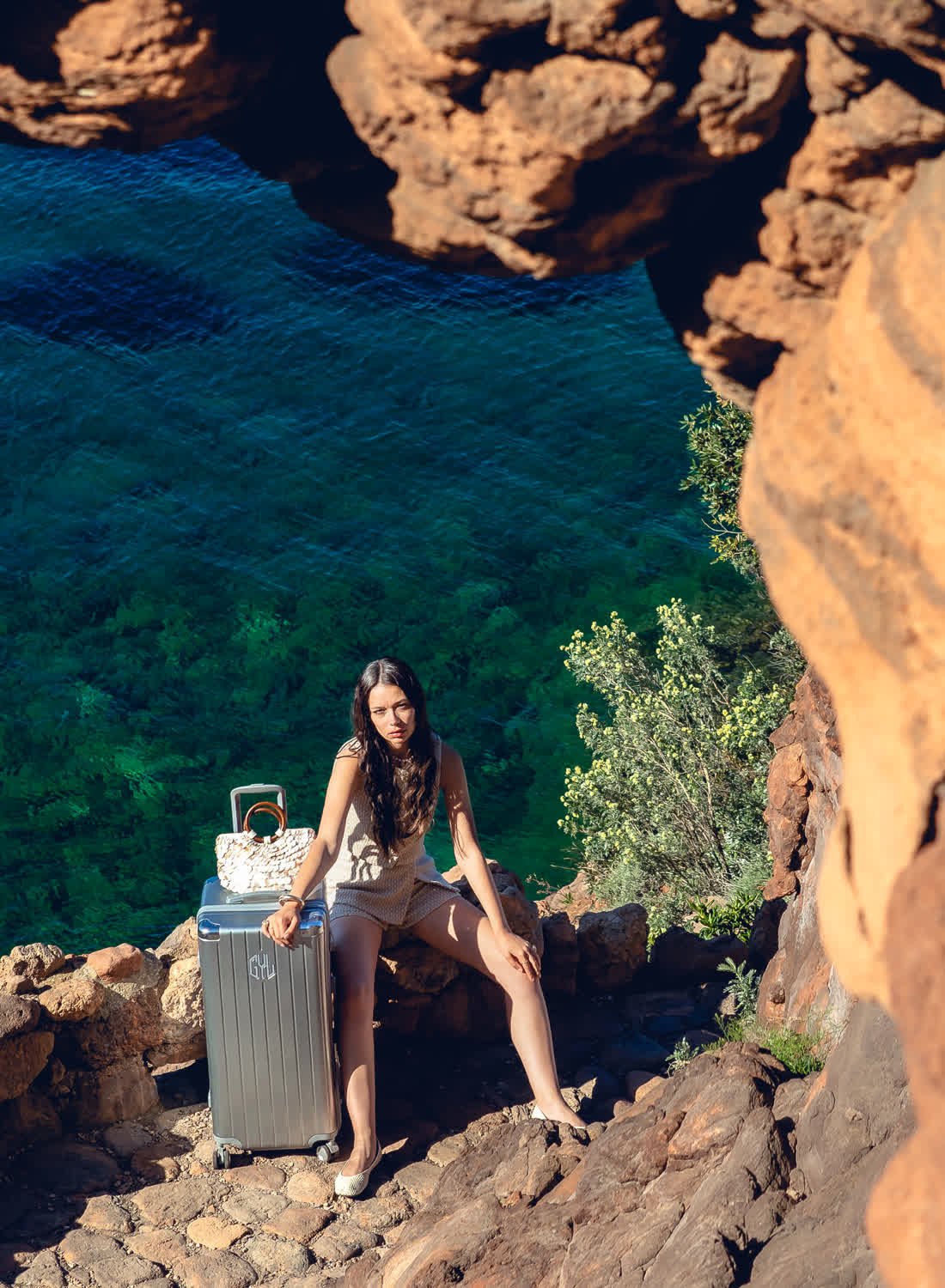 Traveler with a GYL trunk suitcase beside a turquoise rocky cove