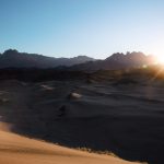 a person is walking in the desert at sunset