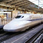 A white Shinkansen bullet train arriving at a modern railway station platform
